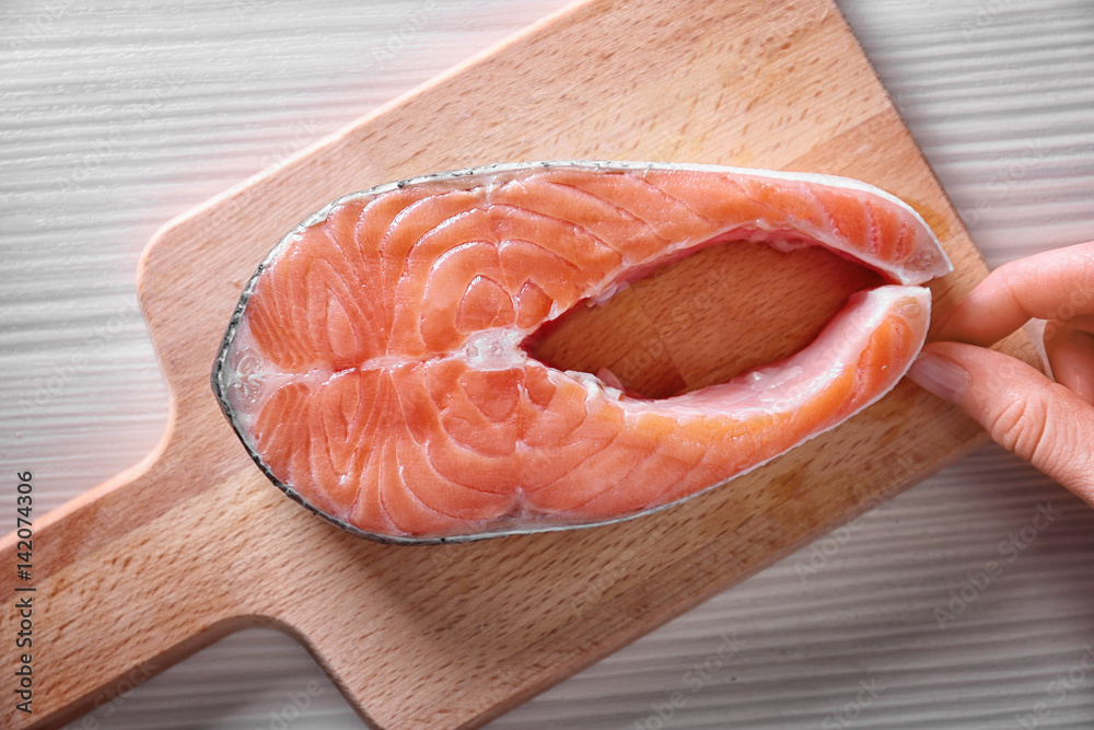 Hand putting fresh salmon steak on wooden cutting board