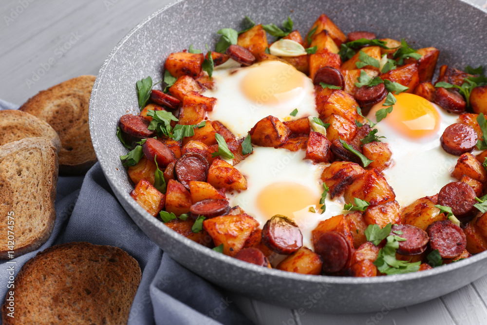 Baked eggs with sausages and potato in pan, closeup
