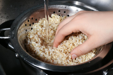 Canvas Print - Female hand washing brown rice with water in colander