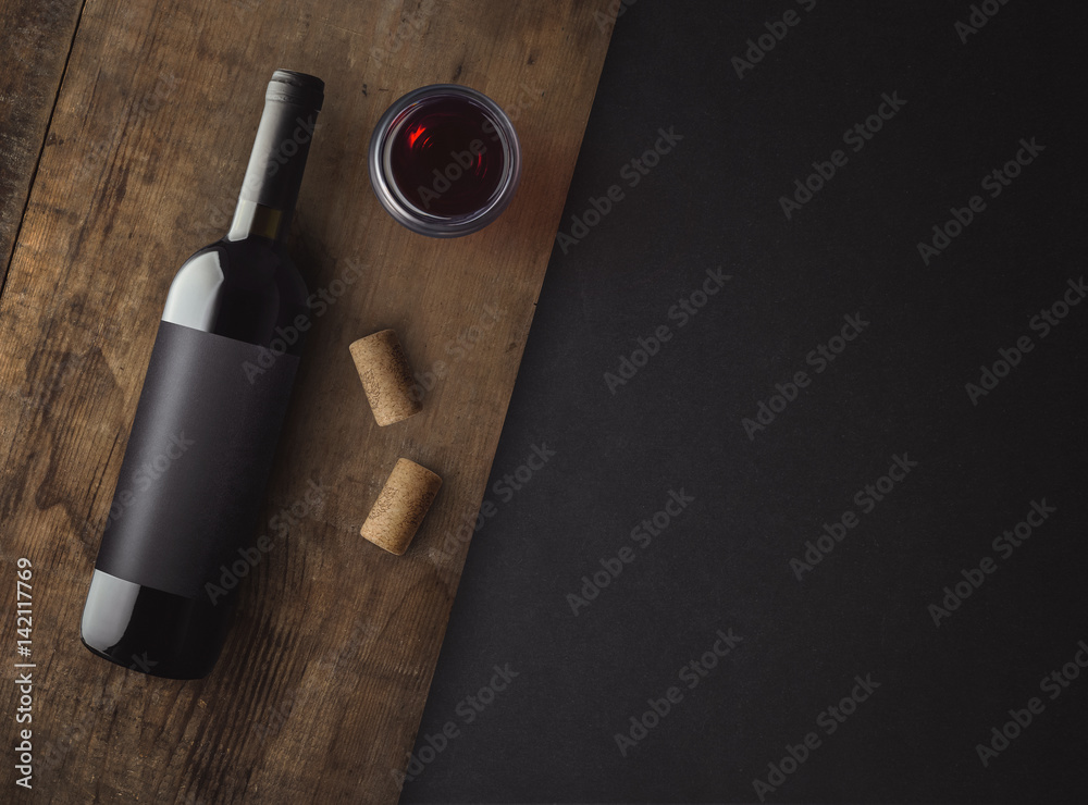 Bottle of red wine with label on old board. Glass of wine and cork. Wine bottle mockup. Top view. - obrazy, fototapety, plakaty 