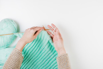 Wall Mural - Top view of a woman hands knitting with wooden needles on white background