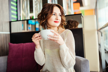 Young woman drinking coffee sitting indoor in urban cafe. Pretty cute girl smiling and holding cup of coffee .