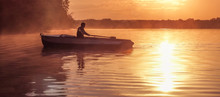 A Young Guy Rides A Boat On A Lake During A Golden Sunset. Image Of Silhouette, Rower At Sunset. Man Rowing A Boat In Backlight Of The Sun
