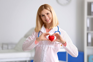 Poster - Female doctor with stethoscope holding heart, on blurred background