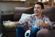 © pressmaster - Portrait of excited man watching sports match on TV and cheering joyfully while eating  popcorn