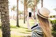 © F8  \ Suport Ukraine - Woman take photo of palm tree and using smart phone outdoor. Black Screen of phone for copy space