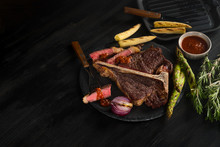 Cooking Steak Porterhouse With Vegetables On A Plate And Pan Grill. Black Table Background With Brown Textile. Copy Text Area For Menu Design. Horizontal Top View, Flat, Overhead.