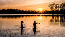 Two Young Kids Are Fishing Under Sunset Of A Lake