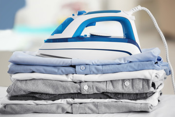 Wall Mural - Electric iron and pile of clothes on blurred background