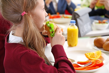 Beautiful girl eating delicious food while sitting at dining table in school cafeteria