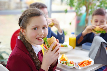 Beautiful girl eating delicious food while sitting at dining table in school cafeteria