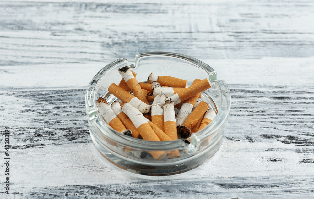 Glass ashtray with cigarette butts on wooden background