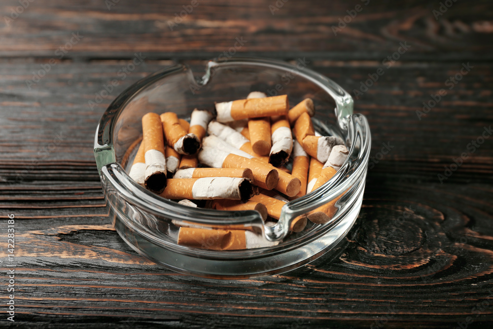 Glass ashtray with cigarette butts on wooden background