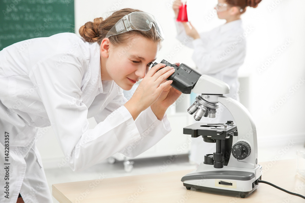 Beautiful school girl looking through microscope in chemistry class