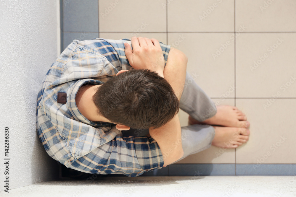 Handsome depressed man sitting on floor at home