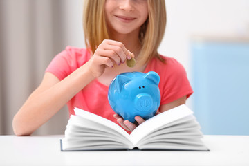 Wall Mural - Cute girl putting coin into piggy bank at home, closeup