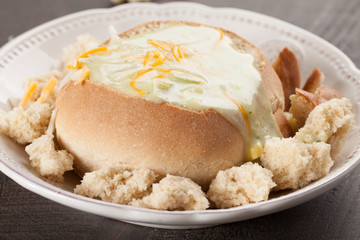 Wall Mural - Creamy Broccoli Cheddar Soup in Large Baked Homemade Roll on white plate on dark wooden background full view of plate