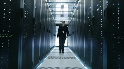 Wall Mural - Frontal View of IT Engineer Walking Through Data Center with Working Rack Servers.   Shot on RED EPIC-W 8K Helium Cinema Camera.