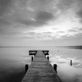 Fototapeta Na drzwi - Stiller See mit Steg bei Sonnenaufgang, wolkiger Himmel, schwarz-weiß