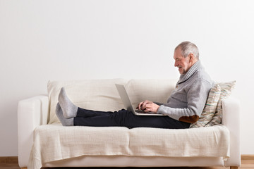 Wall Mural - Senior man sitting on sofa, working on laptop.