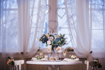 Served table with bouquet of spring flowers. Interior design of white room with beautiful decor. Big windows at the background. Frontal.