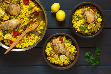 Wall Mural - Chicken paella, a traditional Valencian (Spanish) rice dish made of rice, chicken, peas and capsicum and served with lemon, photographed on dark wood with natural light