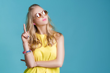 portrait of beautiful blond woman in sunglasses and yellow shirt on blue background. Carefree summer.