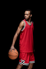 Young african american sportsman standing with basketball ball on black