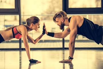 Young sporty man and woman doing plank exercise and giving high five