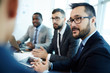 © pressmaster - Portrait of middle-aged Asian businessman in eyeglasses sitting at meeting table and listening to his male colleague with attention, profile view