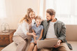 © LIGHTFIELD STUDIOS - Happy family sitting on sofa and using laptop at home