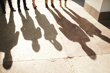 Shadows of five businesspeople standing outdoors, bright sunbeams illuminating shabby asphalt surface