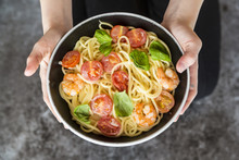 Hands Holding Bowl Of Spaghetti With Prawns, Tomatoes And Basil