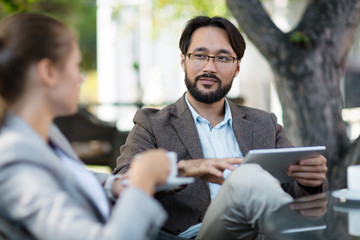 Poster - Productive brainstorming with colleague: Asian businessman and pretty young businesswoman having project discussion while drinking coffee in outdoor cafe