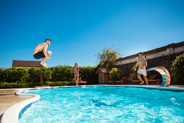 Wall Mural - Young cheerful friends smiling, relaxing, jumping in swimming pool.