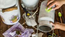Decorating Old Milk Churns With Lavender Pattern - Decoupage Accessories (brush, Scissors, Tissues, Sponge, Paint) And Hands Of An Artist On A Table. High Angle View.