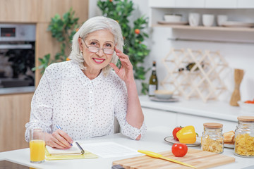 Cheerful senior housewife calculating domestic expenses