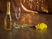 Bottle Of Champagne Two Glasses And Bunch Of Daffodils On A Wooden Surface.
