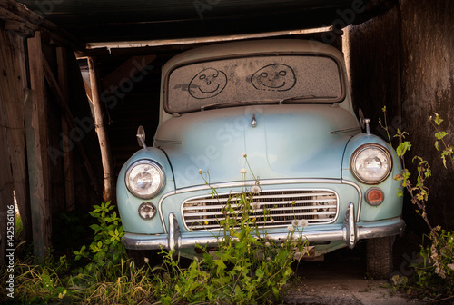 Fotografía Abandoned classic car in overgrown garage with smiling faces drawn in the dusty