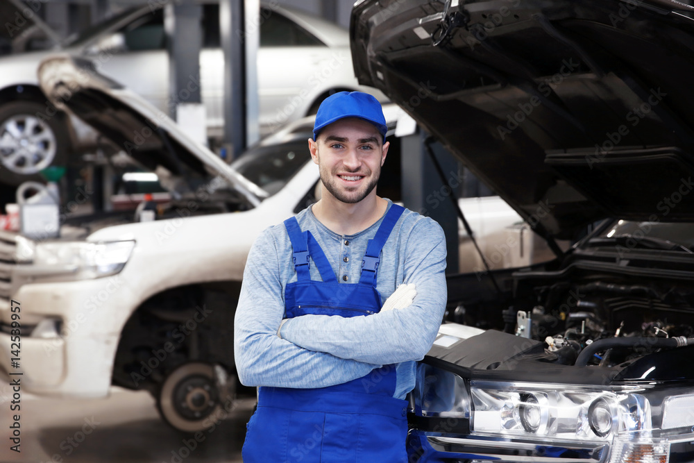 Young mechanic standing in front of open car hood