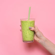 Woman hand holding smoothie shake against pink wall. Drinking green healthy smoothie concept..