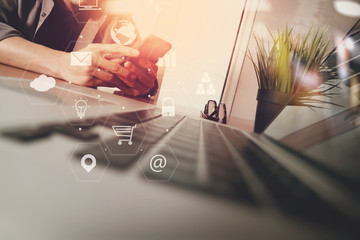 Poster - businessman working with smart phone and laptop computer on wooden desk in modern office with virtual icons interface