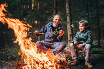 father and son roast marshmallow candies on campfire
