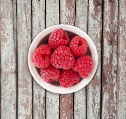 Raspberries in a white ceramic bowl. Ripe and tasty raspberries isolated on a wooden background. Top view.