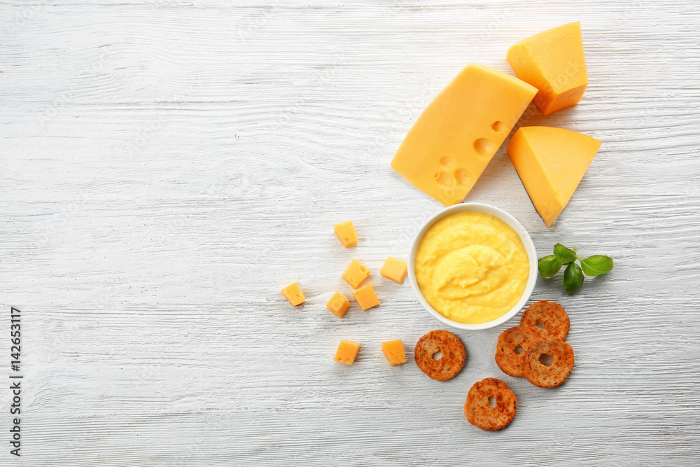 Bowl with cheese sauce and snack on light wooden background