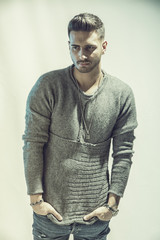 Wall Mural - Handsome young man wearing grey sweater and ripped jeans, on light background in studio shot