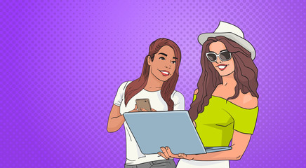 Poster - two young woman using cell smart phone and laptop computer over pop art colorful retro style backgro
