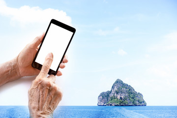 Wall Mural - Always Connected, older person, hand holding and touch smart phone with blank white screen isolated, island seascape background, double exposure