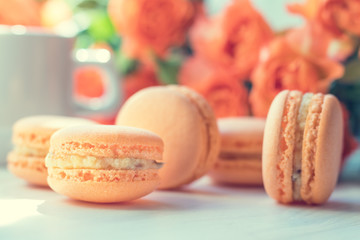 Orange mango or citrous macaroons and orange fresh little roses on light wooden background. Coloring and processing photo with light vintage style. Toned. Shallow depth of field.