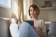 © chika_milan - Pretty businesswoman drinking coffee, using tablet and sitting on couch in pause form freelance work